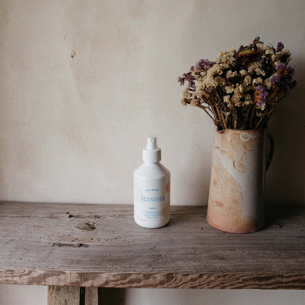 Minois Paris Light Water 250 ml spray bottle on rustic wooden table beside a vase of dried flowers