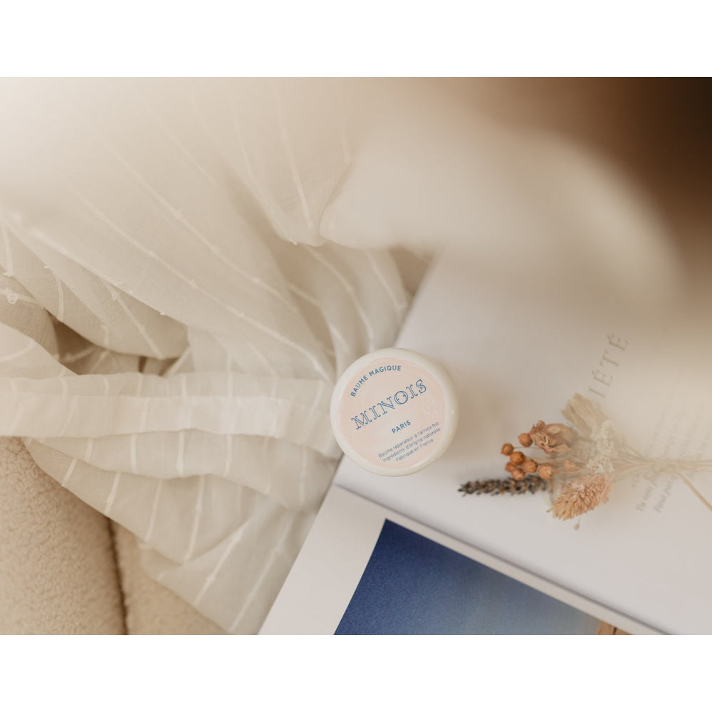 Minois Paris Magic Balm 50g tin with pink label beside dried florals on a white magazine page