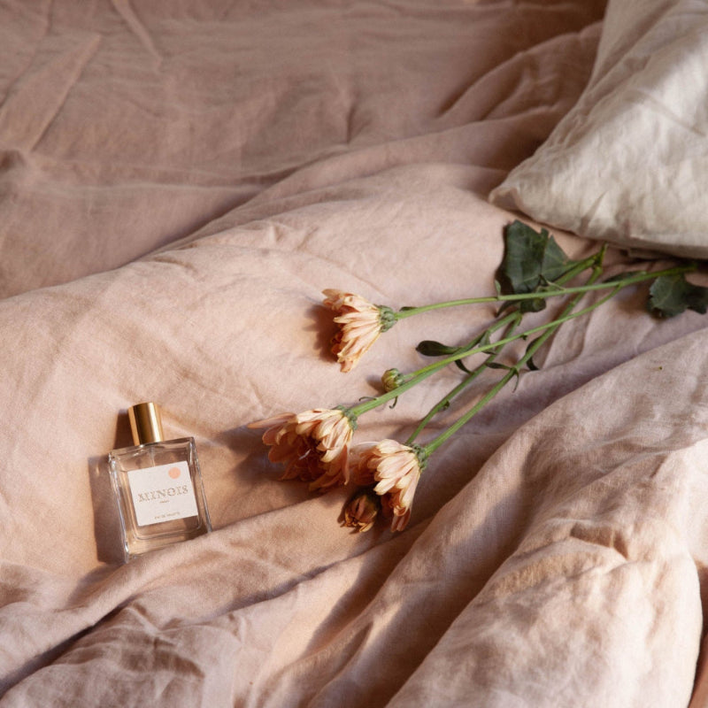 Minois Paris perfume bottle 50 ml with gold cap beside peach chrysanthemums on pale pink fabric