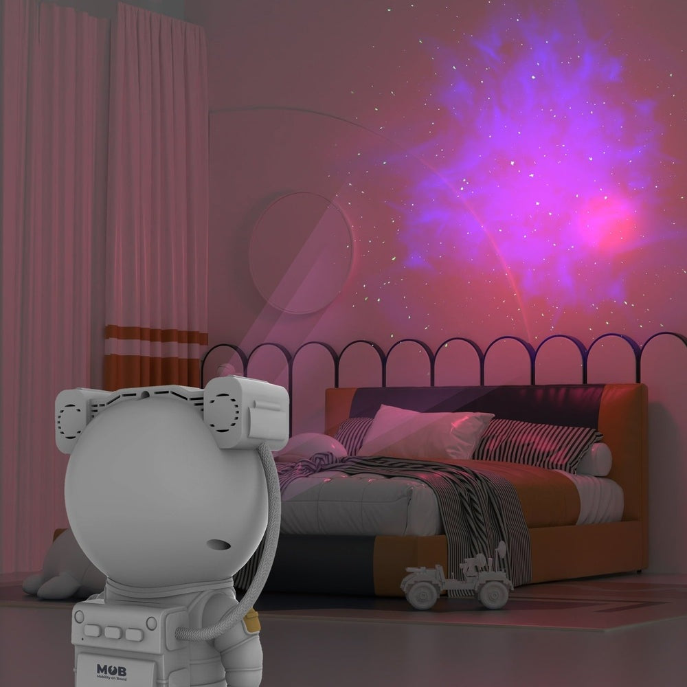Mob Galaxy Light Projector in white projecting pink galaxy onto bedroom wall above bed