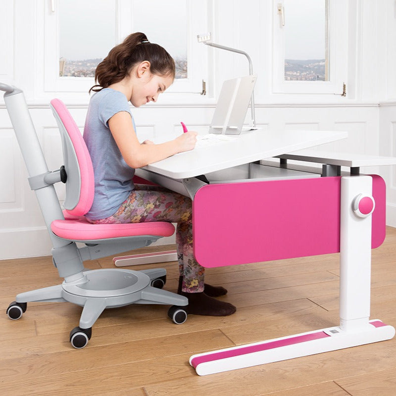 Moll Champion Height Adjustable Desk Front Up in pink and white, where a girl writes at an adjustable-height study desk.