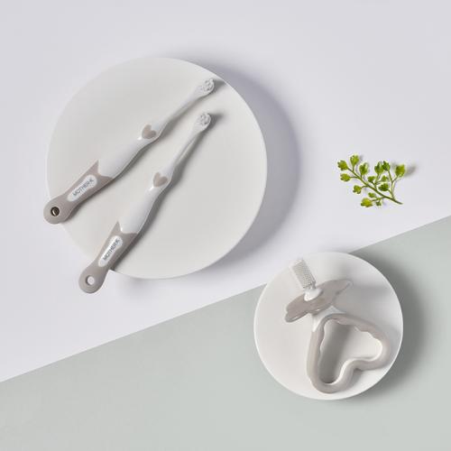 Mother-K Baby Toothbrush 2‑Set with white handles and gray accents, shown with a silicone teether on a plate