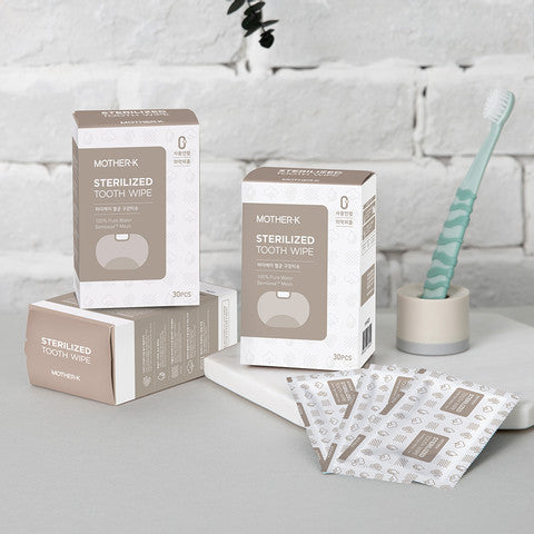 Mother-K sterilized tooth wipes for babies; 3-pack boxed set with beige labels, toothbrush visible in background.