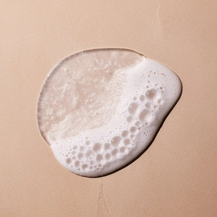 Mustela 2 In 1 Cleansing Gel with Avocado, creamy white foam spread on a beige surface, 500 ml.