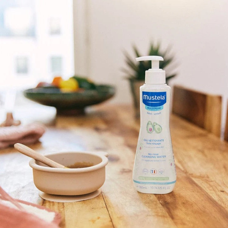 Mustela Baby Cleansing Water No-Rinse with Organic Avocado bottle on a wooden table with pump dispenser.