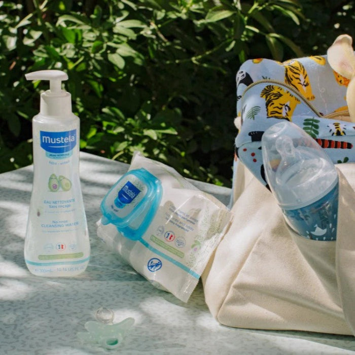 Mustela Baby Cleansing Water Without Rinsing 300 ml bottle with pump, beside wipes in a tote.