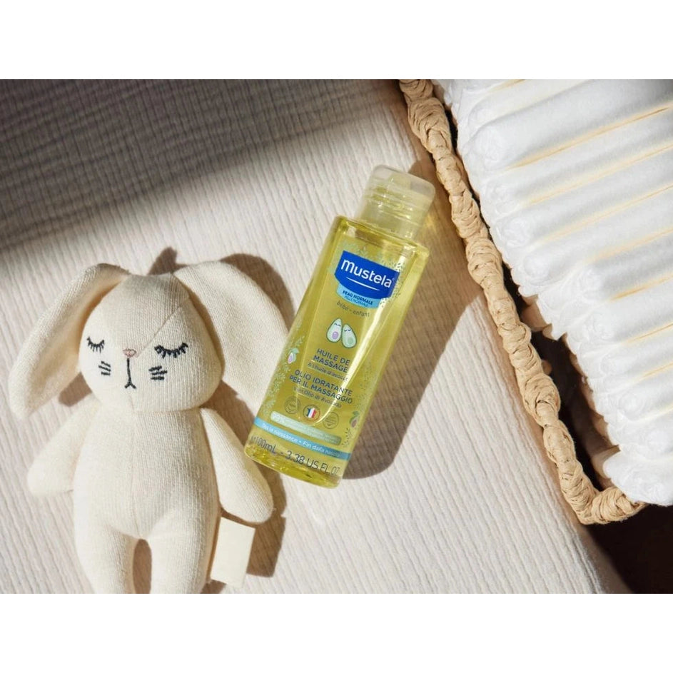 Mustela Baby Massage Oil with Avocado 100 ml bottle beside a white plush bunny