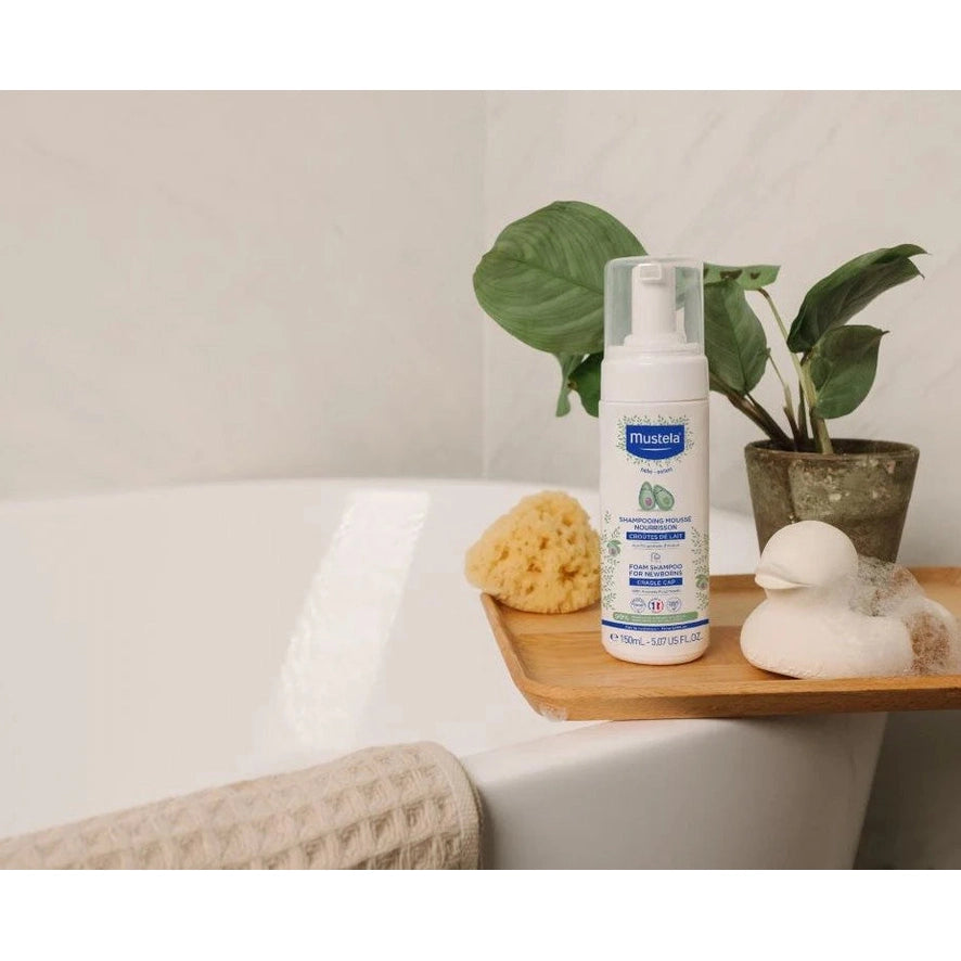 Mustela Infant Foam Shampoo 150 ml bottle on wooden bath tray with sponge and plant