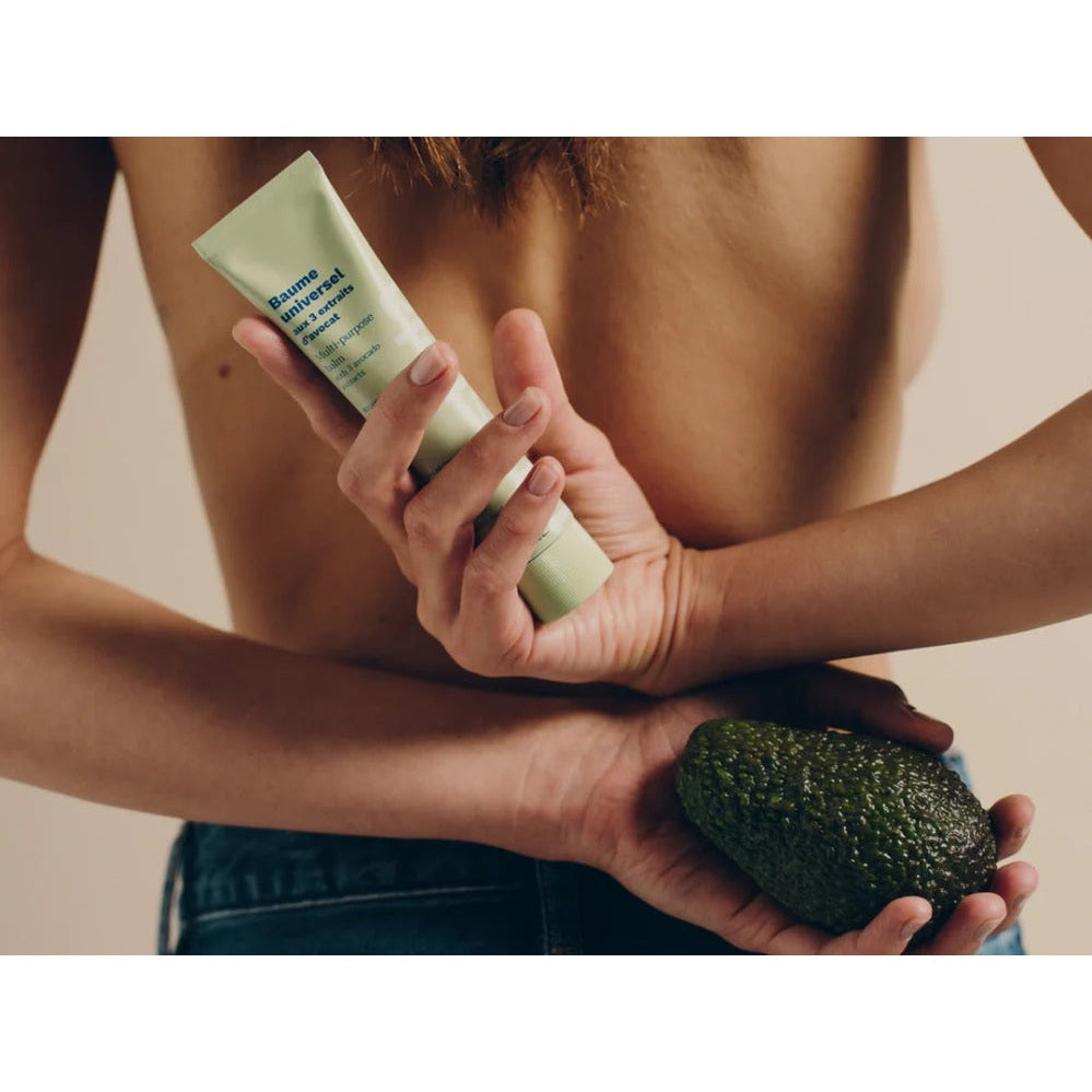 Mustela Organic Universal Balm With 3 Avocado Extracts 75 ml; a person holds the balm tube and an avocado.