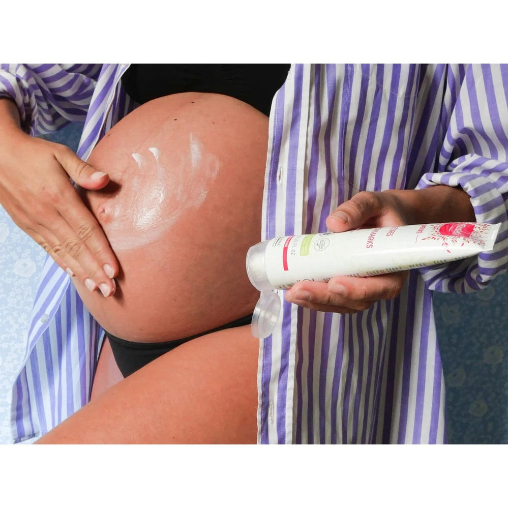 Mustela Stretch Marks Cream 150 ml applied to a pregnant belly; purple striped shirt visible