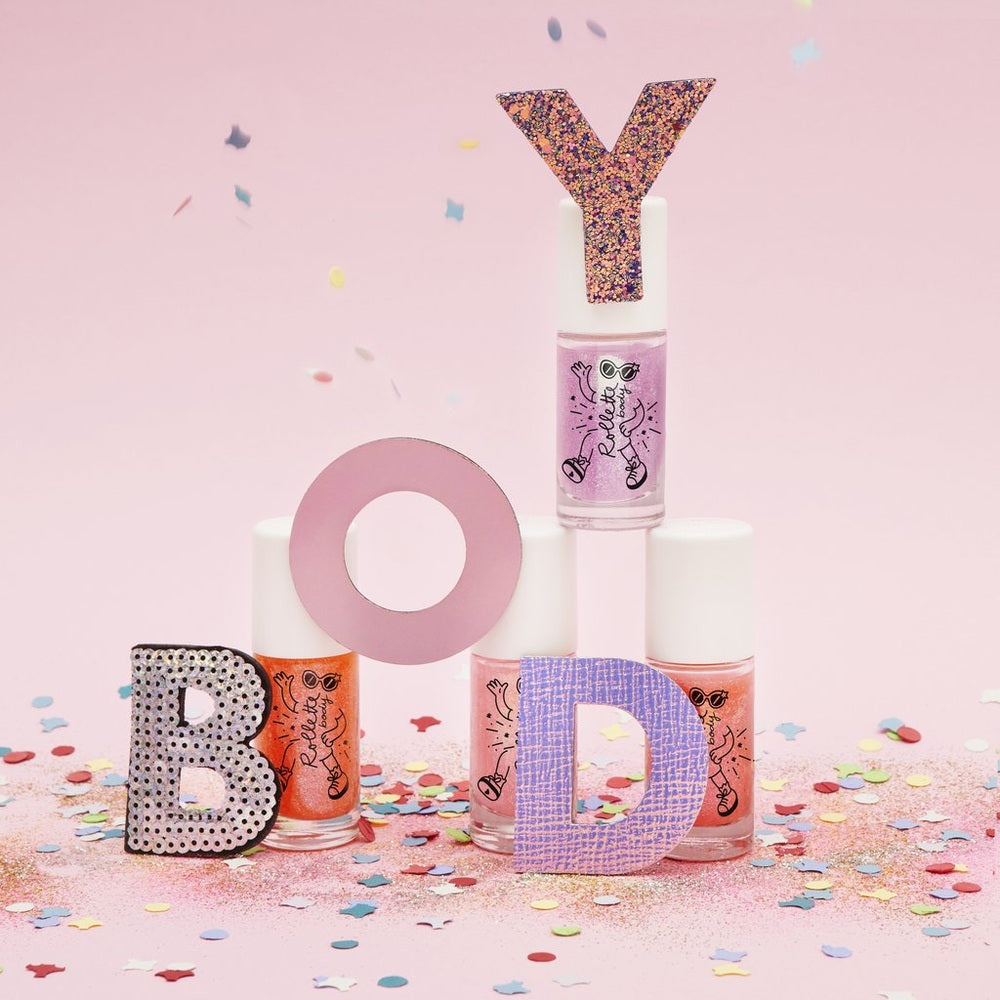 Nailmatic Cherry Body Gel bottle with glittery Y topper beside four pastel polishes spelling BOY on pink backdrop