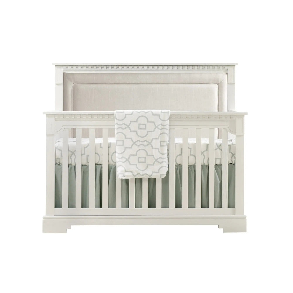 Natart Ithaca 5-In-1 Convertible Crib with Upholstered Headboard, white finish, blanket draped over rail.