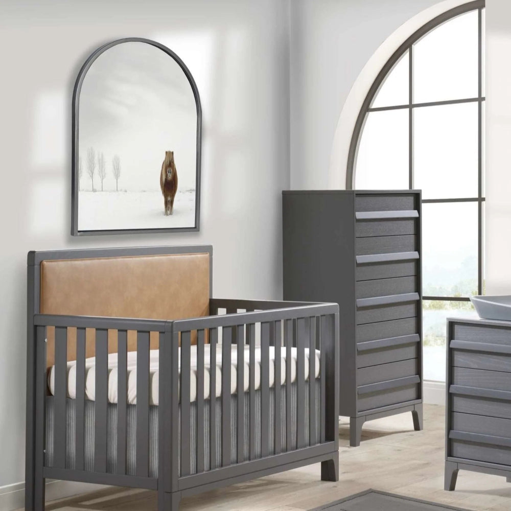 NATART Kyoto 5-in-1 convertible crib with gray frame and tan upholstered panel in a modern nursery.
