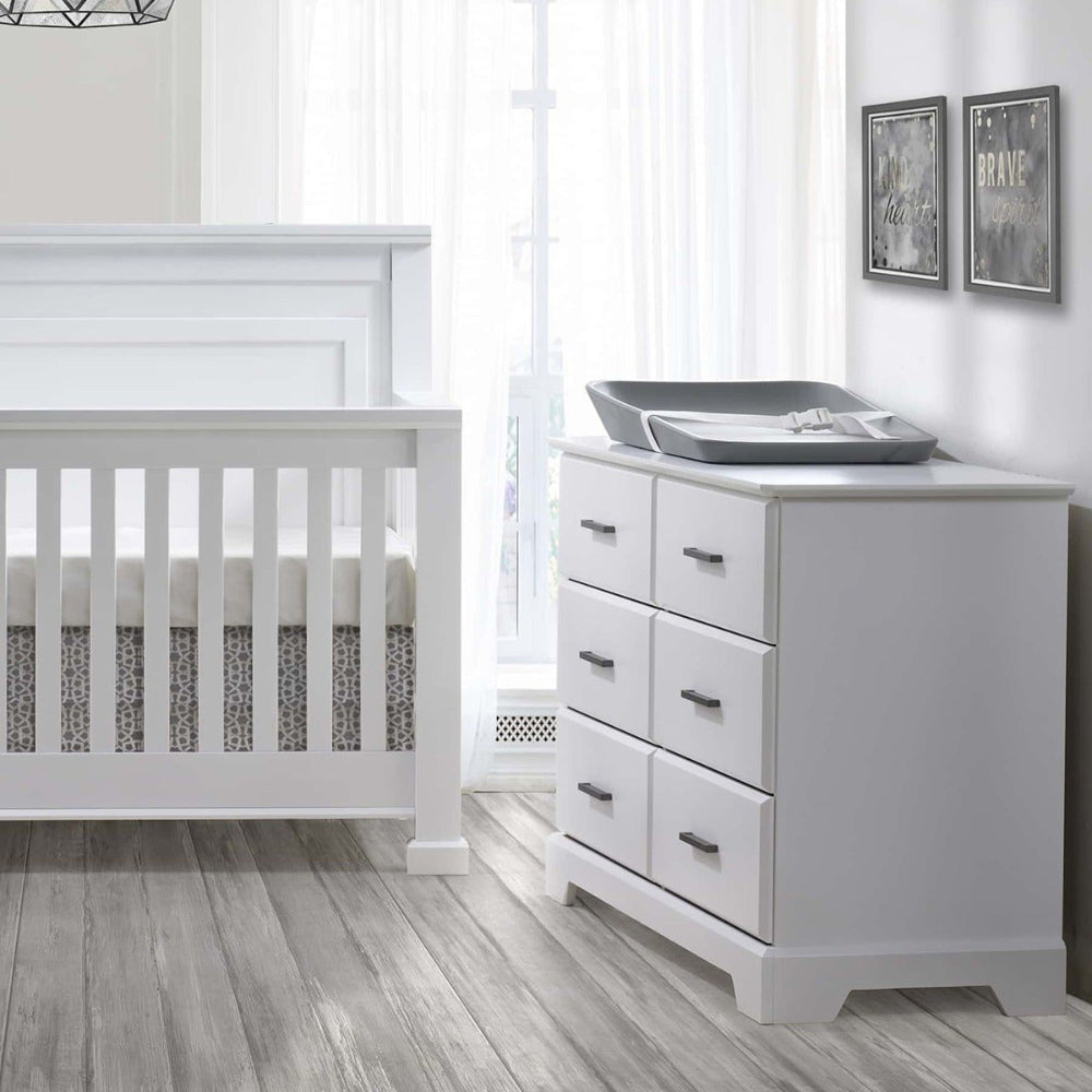 Natart Taylor 5 In 1 Convertible Crib in white with matching dresser and changing pad on top.