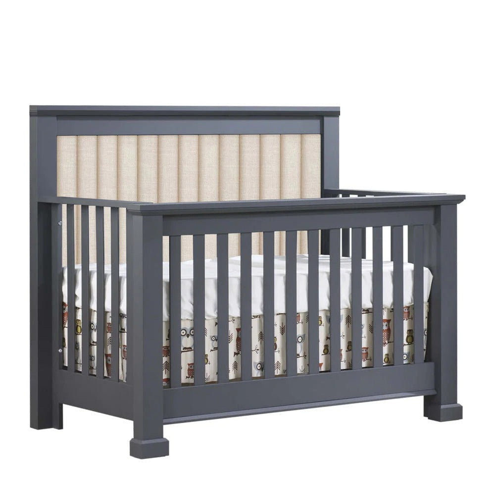 Natart Taylor 5-in-1 convertible crib in dark gray with beige channel-tufted headboard panel.