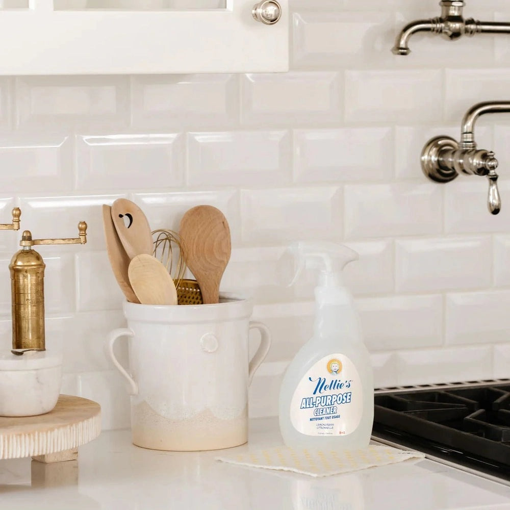 Nellie's All Purpose Cleaner 710 ml bottle on a white kitchen counter next to a mug with wooden utensils, ready to spray.