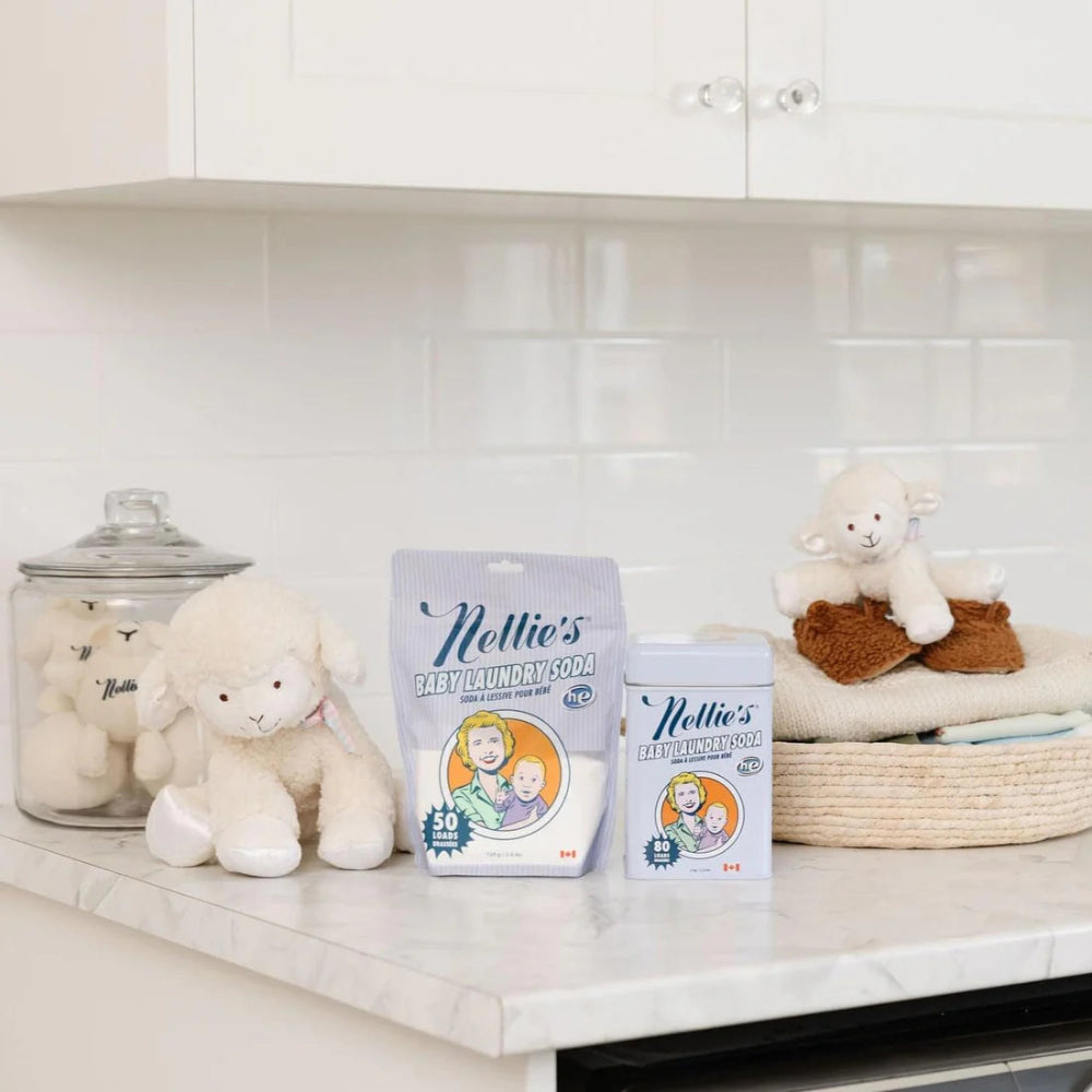 Nellie's Baby Laundry Soda bag and canister on a white kitchen counter with plush sheep toys