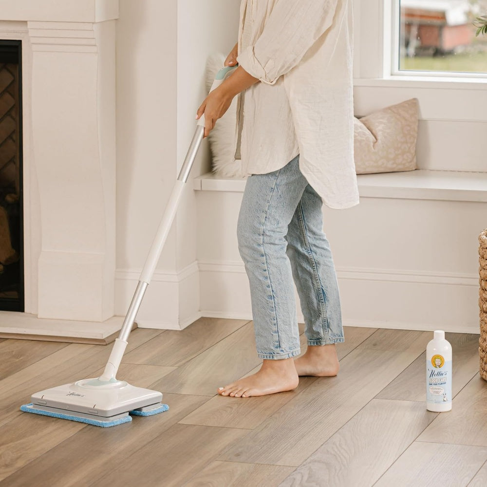 Nellie's Wow Mop cleans light hardwood floors with a blue pad; Nellie's cleaner bottle sits nearby.
