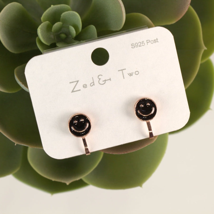 Nemibaby Earrings Smile, rose-gold posts with black enamel smiley faces mounted on a display card.