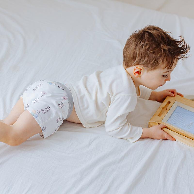 Nest Designs bamboo boys boxer briefs To Infinity, light blue with playful print; toddler crawls on bed inspecting a wooden frame.