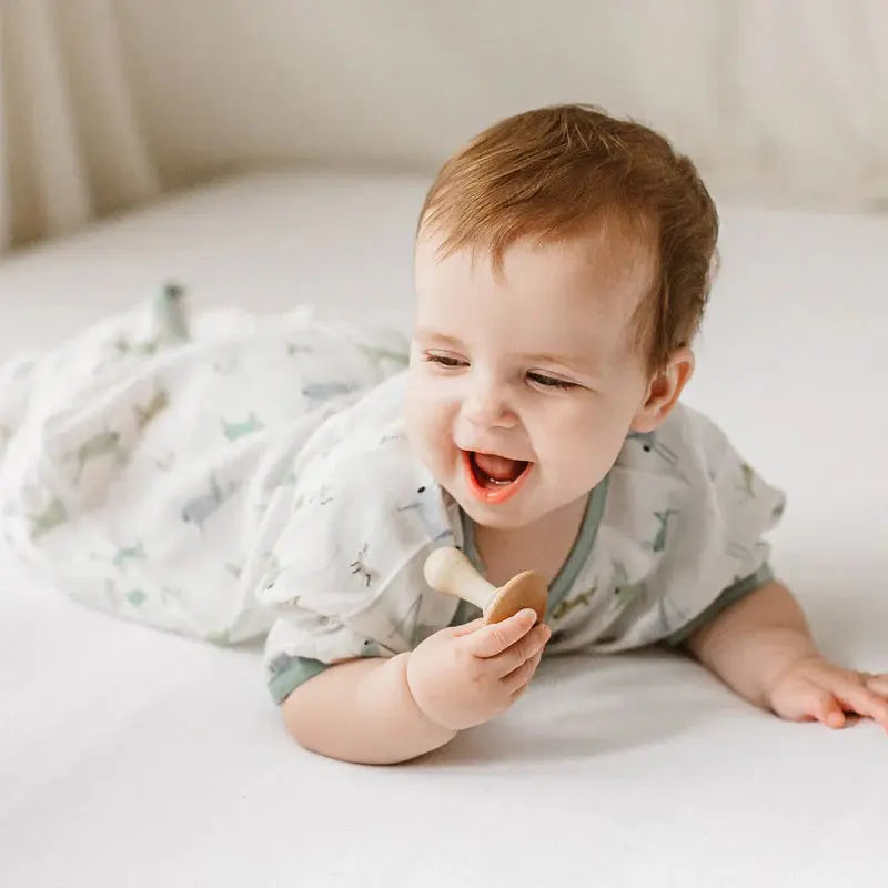 Nest Designs The Ant & The Grasshopper bamboo silk short-sleeve sleep bag 0.23 tog, baby on tummy holding a teether.
