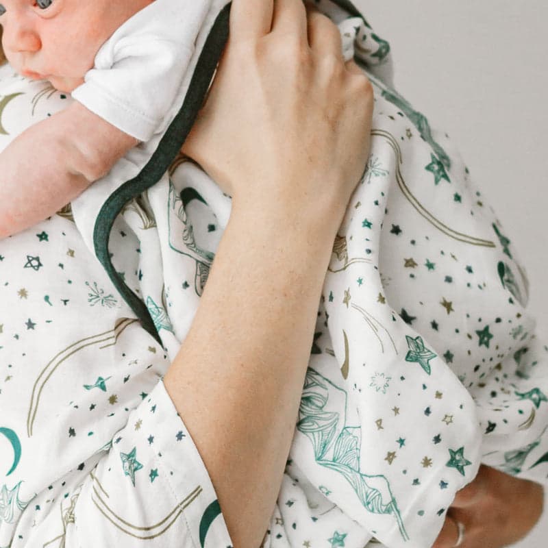 Nest Designs 4-layer bamboo baby blanket, white with teal stars, wrapped around baby