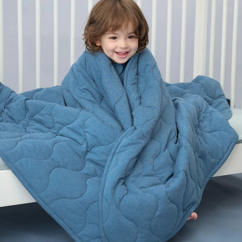 Nest Designs Avocado Bamboo Cozy Blanket Medium Captain's Blue wraps a smiling toddler in a crib.