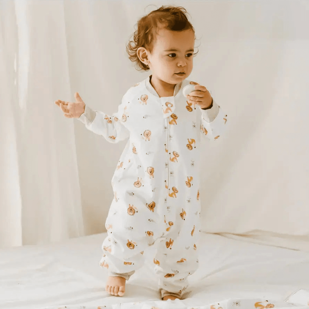 Nest Designs Avocado Bamboo Long Sleeve Footed Sleep Bag 1.0 Tog The Lion & The Mouse; toddler stands in a white sleep sack.