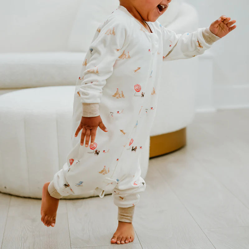 Nest Designs Avocado Bamboo long-sleeve footed sleep bag, Beach Daze print, white, 1.0 TOG; toddler walking indoors shows footed design.