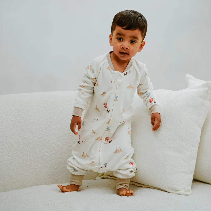 Nest Designs Avocado Bamboo Long Sleeve Footed Sleep Bag 1.0 Tog Beach Daze; baby stands on couch in cozy footed sleepwear.