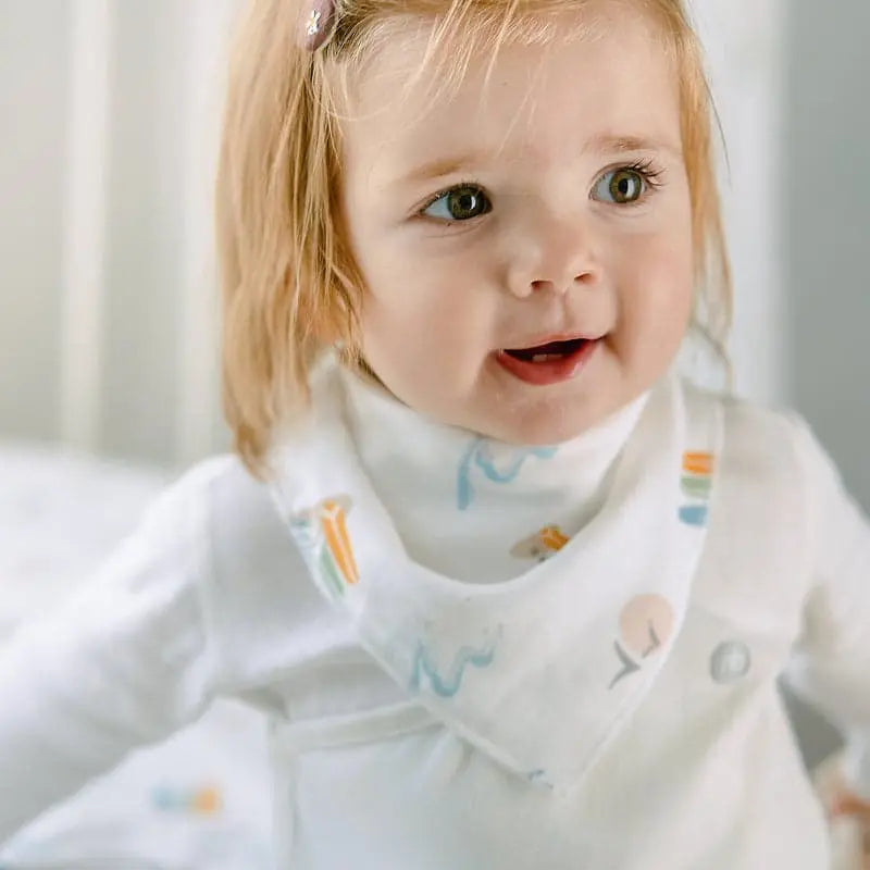 Nest Designs Bamboo Baby Bandana Bib, one size, worn by a smiling toddler in white with pastel prints.