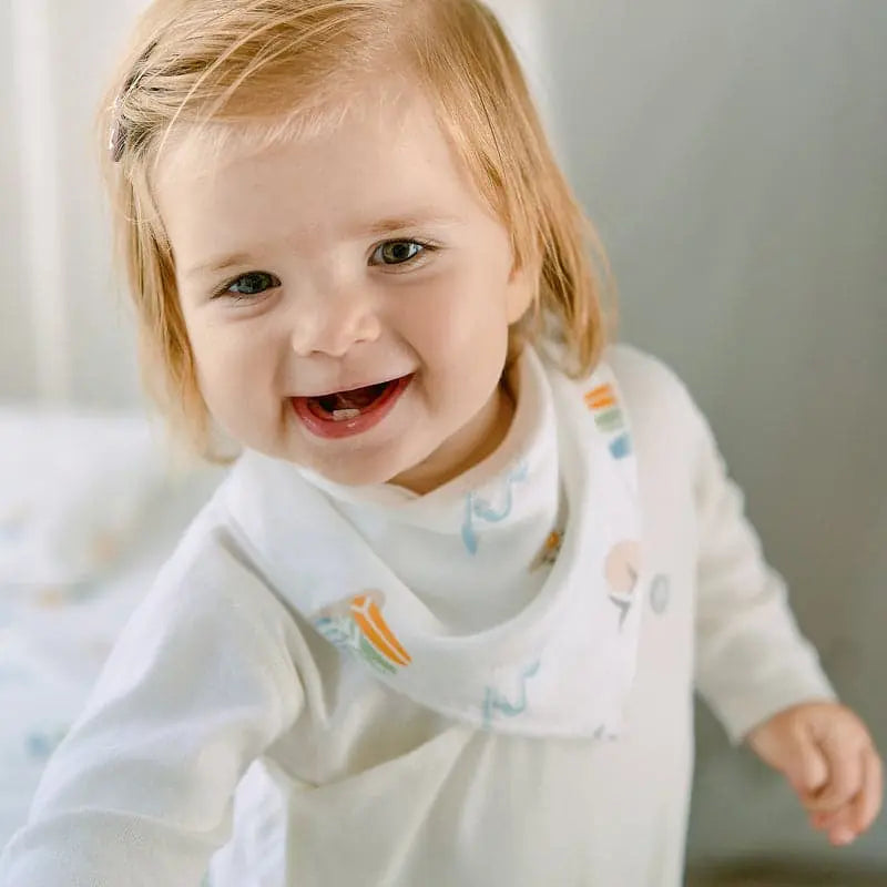 Nest Designs Bamboo Baby Bandana Bib One Size (3M-24M) on a smiling baby in white with pastel prints.