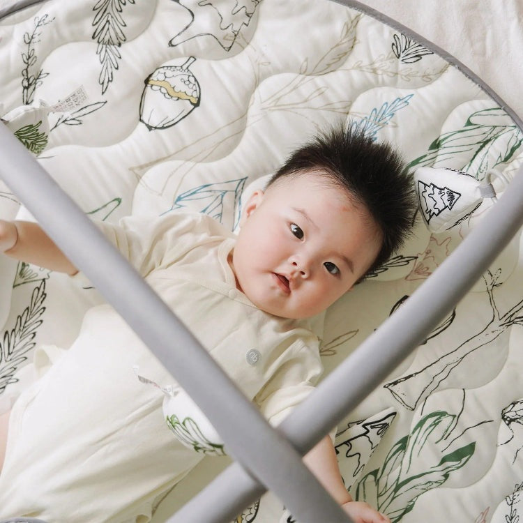 Nest Designs Bamboo Baby Play Mat and Activity Gym, Fresh Forest design, cream mat with forest print and a baby lying on it