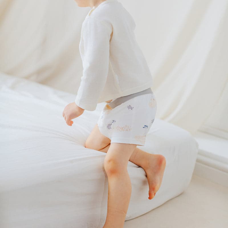 Nest Designs Bamboo Boys Boxer Briefs 2-Pack Savanna Secrets; toddler climbs onto a white bed, showing soft fabric and pastel print.