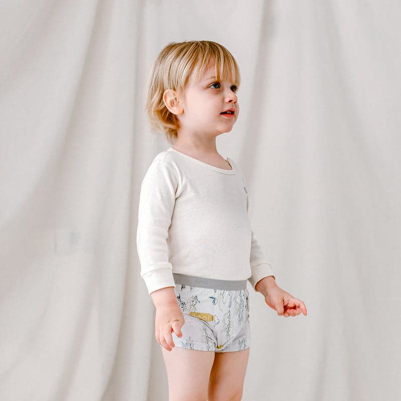 Nest Designs Bamboo Boys Boxer Briefs Underwear 2-Pack; toddler in white shirt wearing gray-blue tree-pattern briefs.