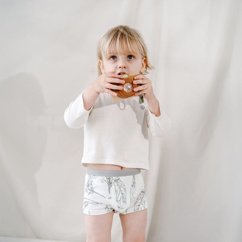 Nest Designs Bamboo Boys Boxer Briefs Underwear (2 Pack) Feather Light; toddler in white top and leaf-print shorts holding a brown toy.