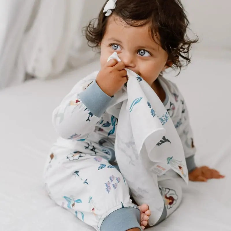 Nest Designs Bamboo Bubs Baby Washcloth Set (6-pack) in white with blue/green prints; baby holds a washcloth to her face.