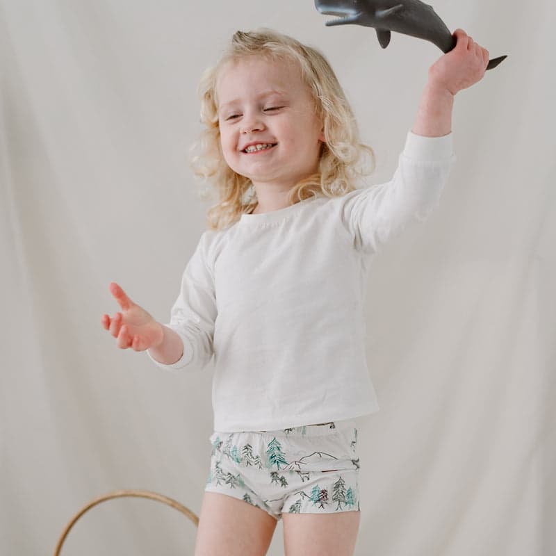 Nest Designs Bamboo Girls Boy Short Underwear Forest Fun 2-pack: joyful girl wears forest-print shorts, raising arm cheerfully.