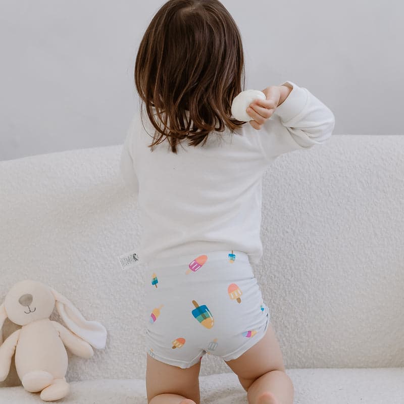 Nest Designs Bamboo Girls Underwear 2 Pack Sweet Treats; toddler in white top wearing popsicle-printed briefs, standing back-to-camera.