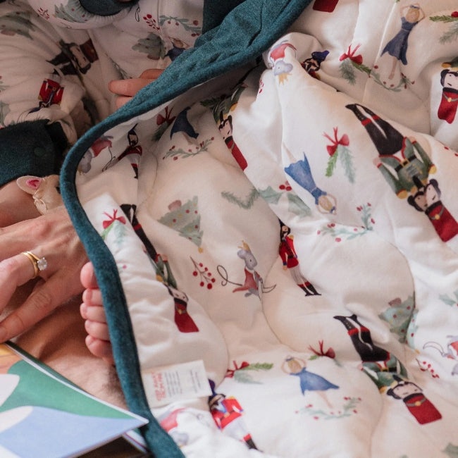Nest Designs Bamboo Jersey Cozy Blanket Medium Nutcracker snuggled around a sleeping baby with teal trim
