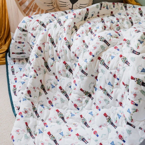 Nest Designs Bamboo Jersey Cozy Blanket Medium Nutcracker draped over a bed with teal trim.