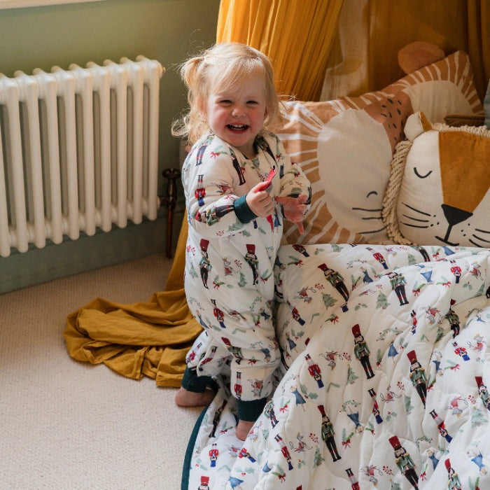 Nest Designs Bamboo Jersey Cozy Blanket Medium Nutcracker draped over bed as toddler plays on it in a cozy nursery.