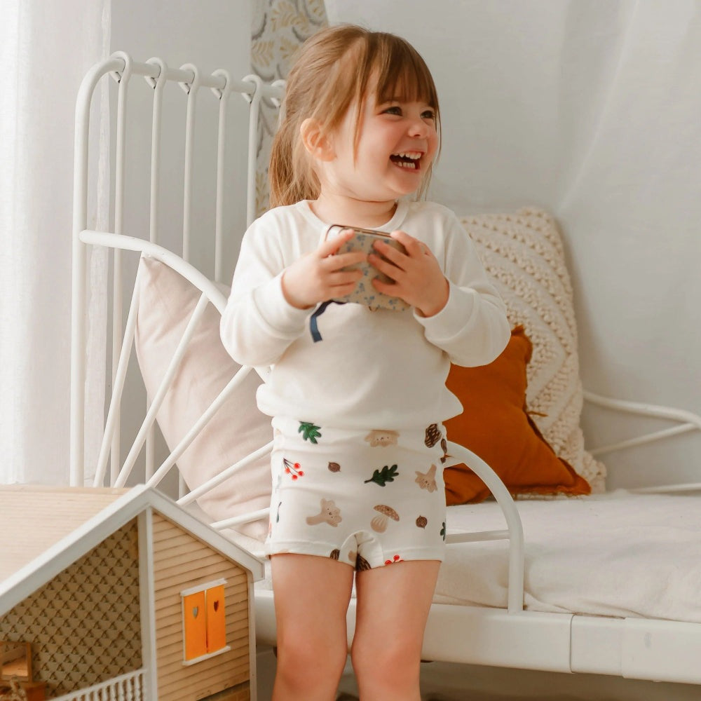 Nest Designs bamboo jersey toddler girl shorts set: white long-sleeve top and printed shorts, holding a cup