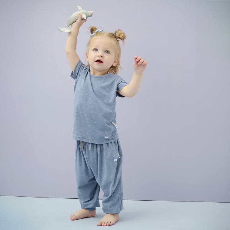 Nest Designs Bamboo Jersey Harem Pants Troposphere for toddlers in blue, worn by a toddler reaching up with a plush shark