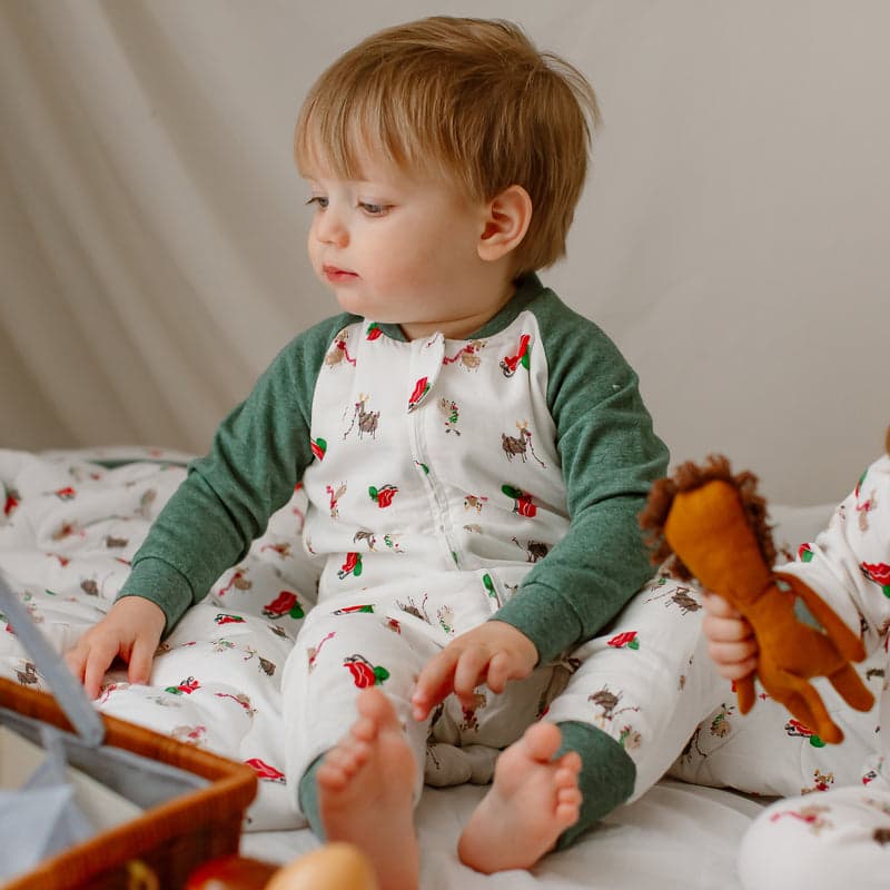 Nest Designs Bamboo Jersey Long Sleeve Footed Sleep Bag 2.5 Tog Sleigh All Day, toddler sits up in bed reaching for a stuffed horse.