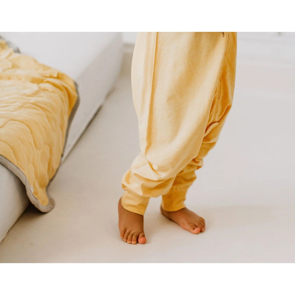 Nest Designs Bamboo Jersey Short Sleeve Footed Sleep Bag 0.5 Tog Pantone Sunset Gold; baby standing in cozy yellow sleepwear.