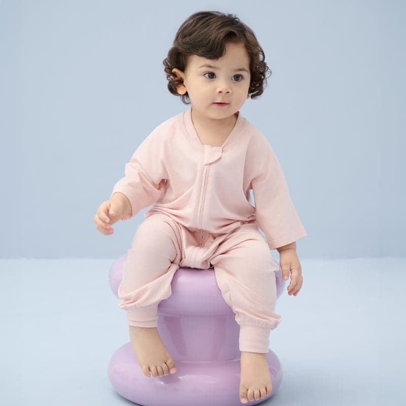 Nest Designs Bamboo Jersey Short Sleeve Footed Sleep Bag 0.6 Tog Rose Smoke; baby sits on a lavender stool.