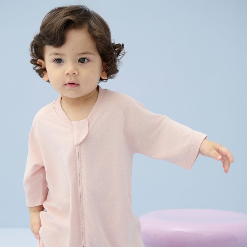 Nest Designs bamboo jersey short-sleeve footed sleep bag 0.6 Tog Rose Smoke; toddler stands with arm outstretched.