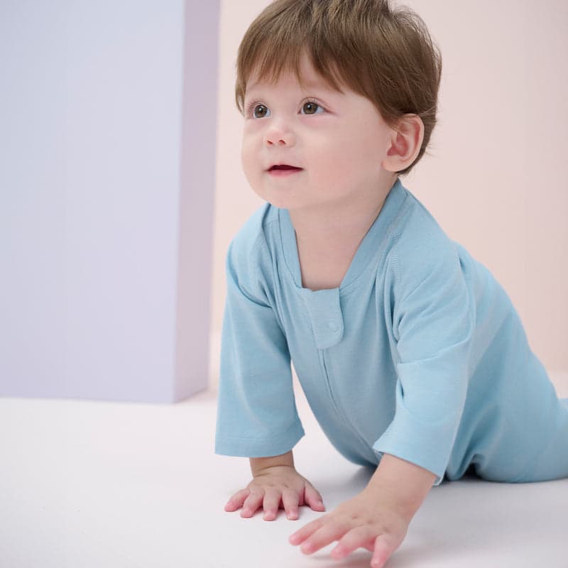 Nest Designs bamboo jersey short-sleeve footed sleep bag 0.6 tog Forget-Me-Not blue, as a baby crawls in its cozy blue sleep sack.