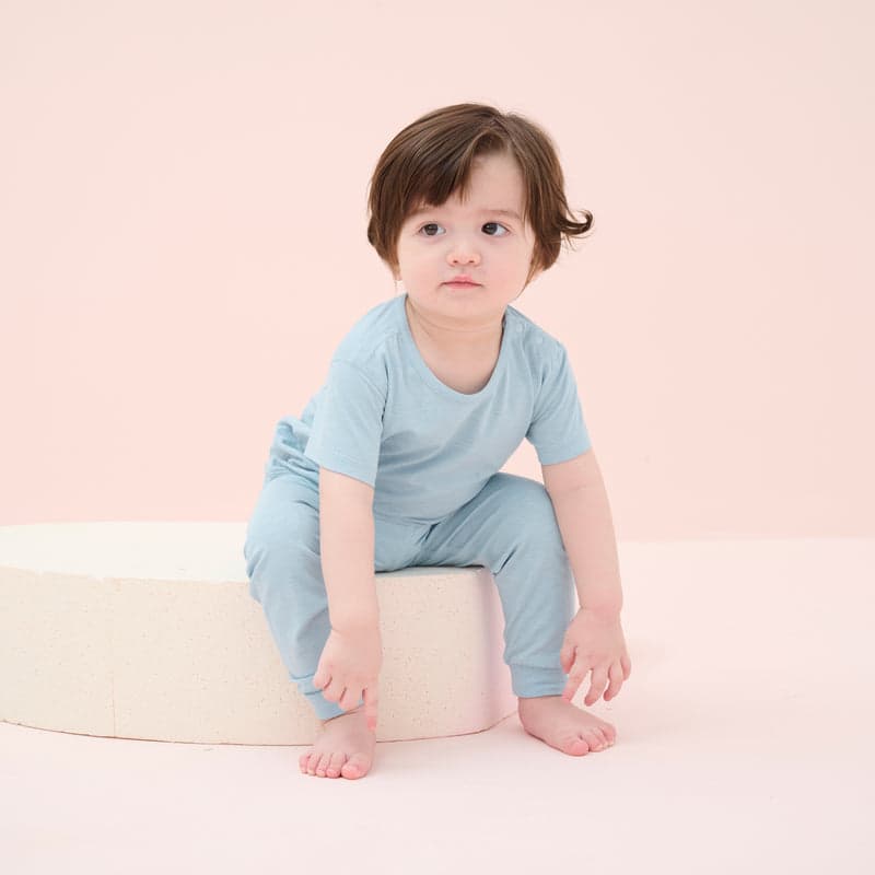 Nest Designs Forget-Me-Not bamboo jersey short-sleeve pajama set worn by a toddler on a curved white platform against a pastel peach backdrop.